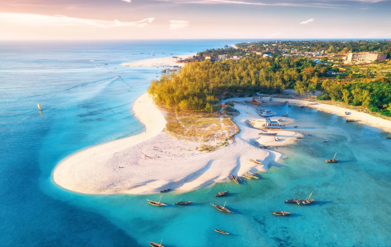 Aerial view of the fishing boats on tropical sea coast with sandy beach at sunset.  Summer travel in Zanzibar, Africa. Top view of boats, yachts, green palm trees, clear blue water, colorful sky photo.
