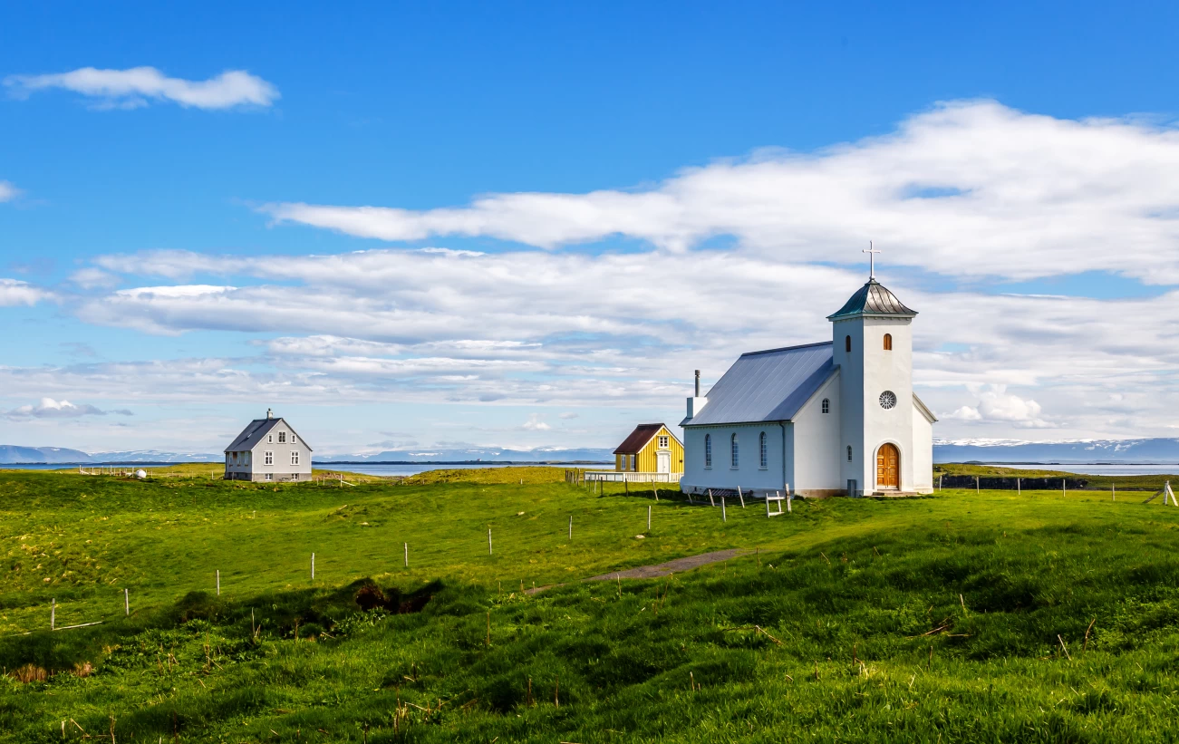 Flateyjarkirkja church and couple of living houses with meadow in foreground and blue sky, Flatey, Iceland