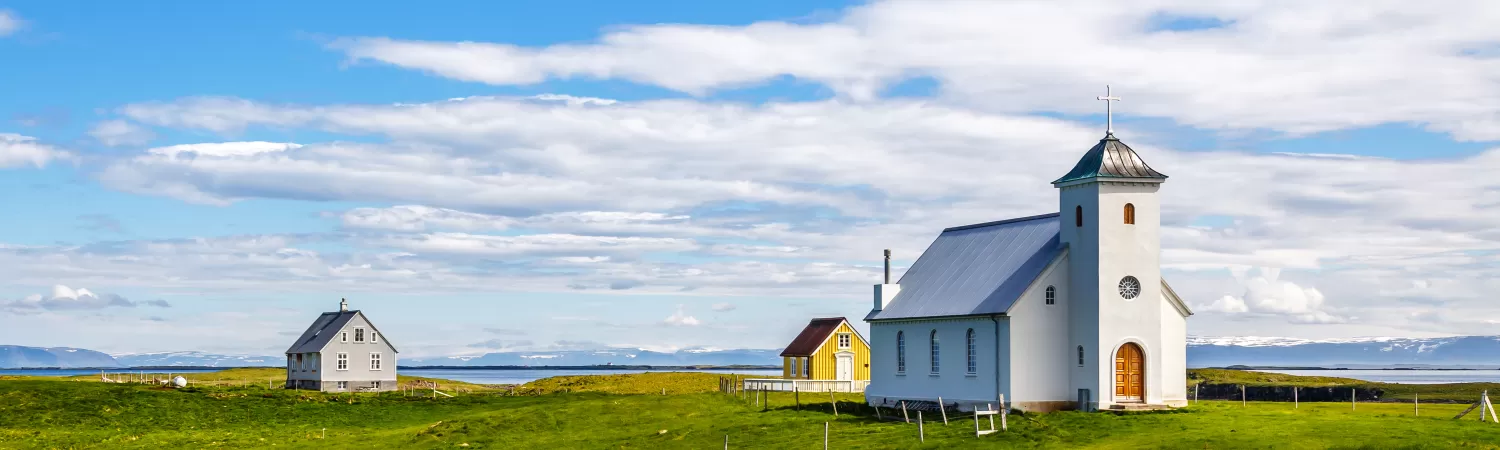 Flateyjarkirkja church and couple of living houses with meadow in foreground and blue sky, Flatey, Iceland