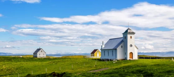 Flateyjarkirkja church and couple of living houses with meadow in foreground and blue sky, Flatey, Iceland