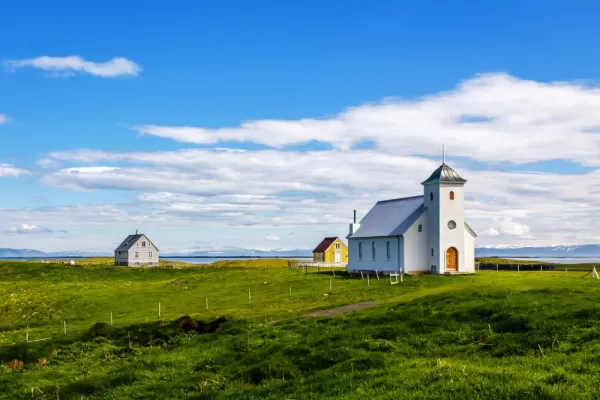 Flateyjarkirkja church and couple of living houses with meadow in foreground and blue sky, Flatey, Iceland
