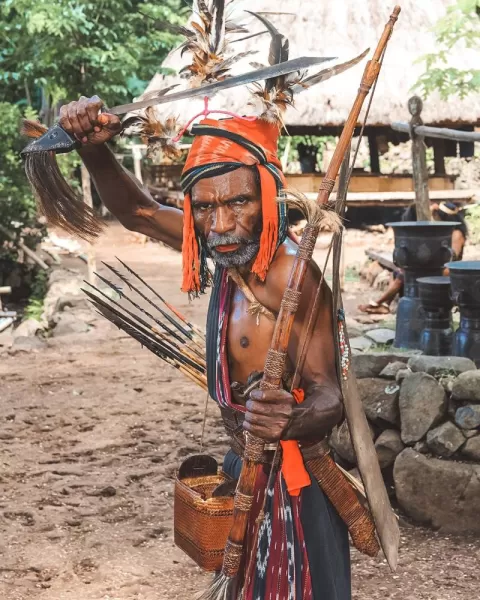 A local Abui elder demonstrates warrior pose with traditional hunting implements.