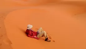 A man rests on the bright red sand of Africa.