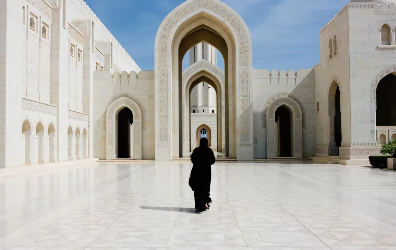 A women in traditional dress walks through the Sultan Qaboos Grand Mosque.