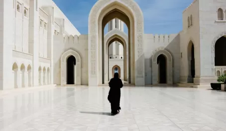 A women in traditional dress walks through the Sultan Qaboos Grand Mosque.