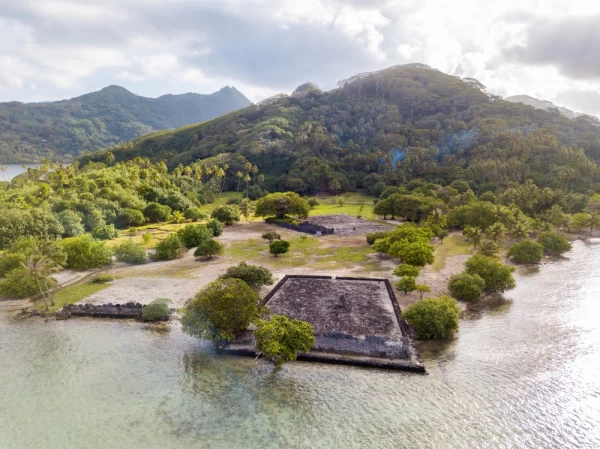 Ancient Marae Taputapuatea temple complex on the lagoon shore with mountains on background. Raiatea island