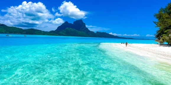 Crystal-clear turquoise waters meet pristine white sand at Bora Bora, with the iconic Mount Otemanu in the background, creating a perfect tropical paradise