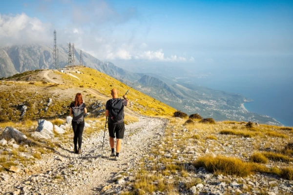 Two hikers on top of a mountain ridge with a vast view of the southern coast of Albania.