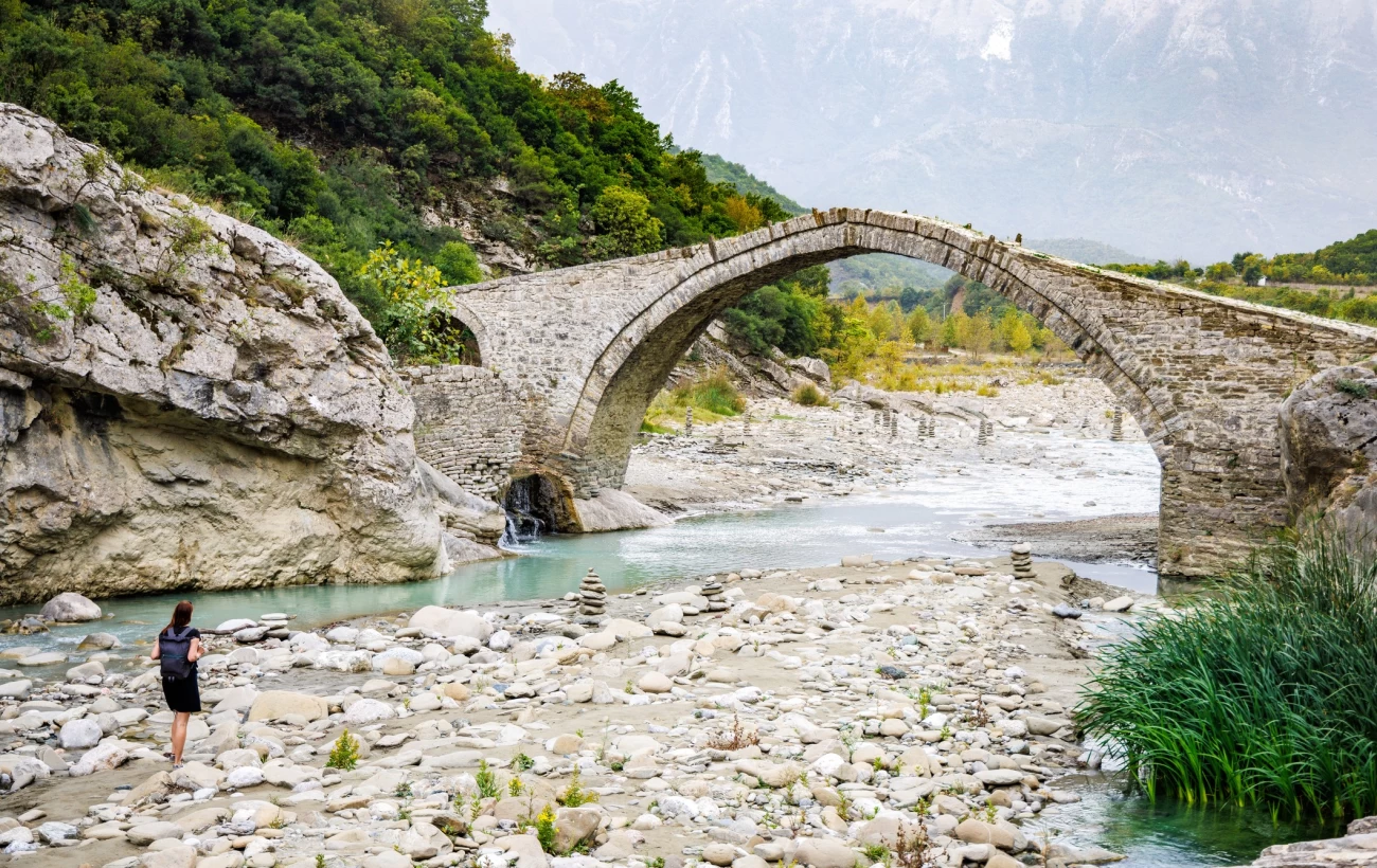 A female tourist is walking on the riverbed next to the historical Ottoman Kadiu bridge in Albania