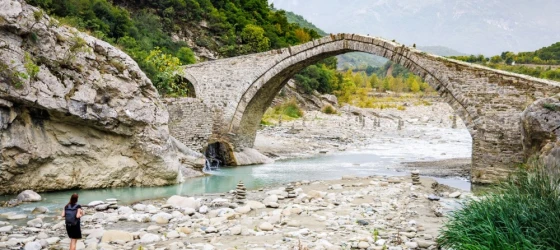 A female tourist is walking on the riverbed next to the historical Ottoman Kadiu bridge in Albania