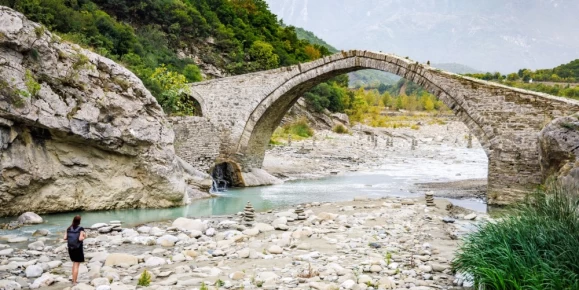 A female tourist is walking on the riverbed next to the historical Ottoman Kadiu bridge in Albania