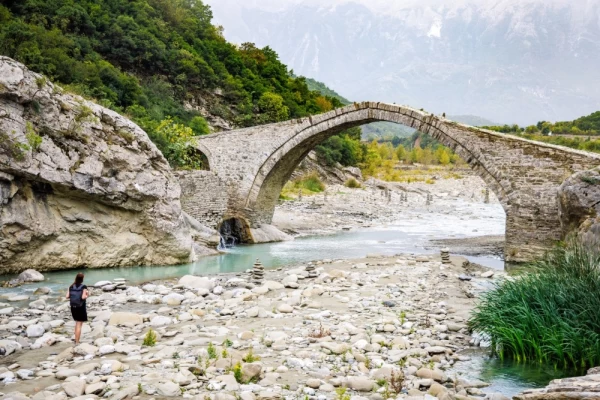 A female tourist is walking on the riverbed next to the historical Ottoman Kadiu bridge in Albania