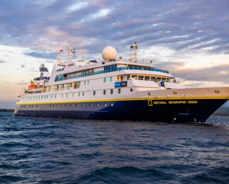 With the sun setting and casting a spectrum of warm hues across the sky, the ship National Geographic Orion