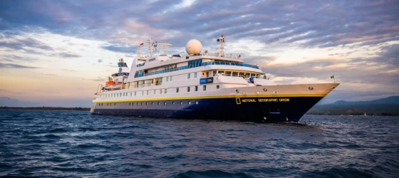 With the sun setting and casting a spectrum of warm hues across the sky, the ship National Geographic Orion