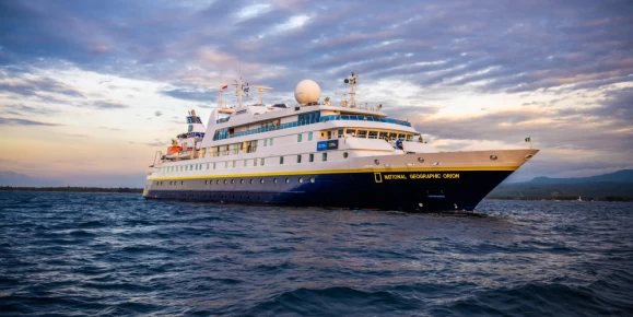 With the sun setting and casting a spectrum of warm hues across the sky, the ship National Geographic Orion