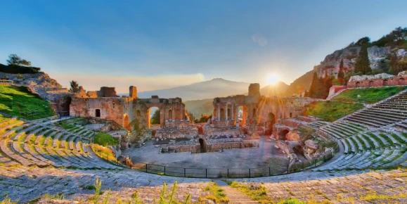 Ancient theater of Taormina Sicily Italy with Etna erupting volcano at sunset
