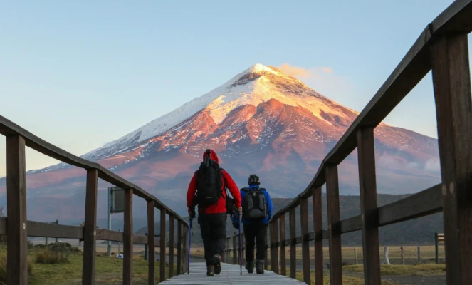 Tourists walking on a wooden boardwalk toward the Cotopaxi volcano