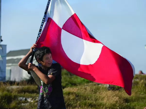 A local boy carries the flag of Greenland.