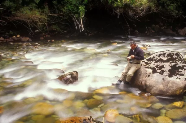 A fly fisherman changes his fly in the rushing river water.