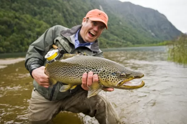 A fly fisherman show off his catch to the camera.