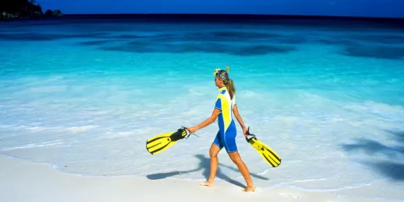 A snorkeler walking along a white sandy beach.