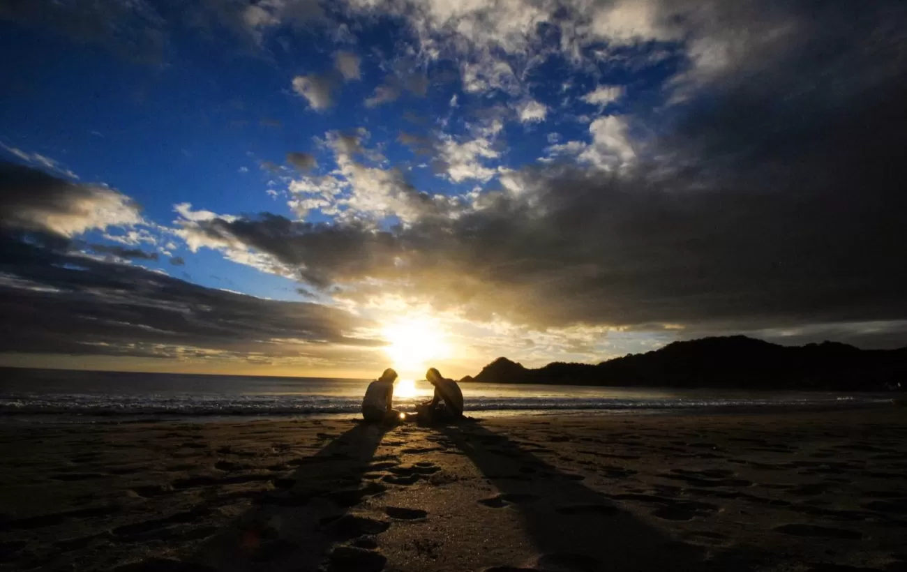 The sun sets behind two travelers enjoying the warm sands of a Nicaragua beach.