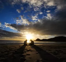 The sun sets behind two travelers enjoying the warm sands of a Nicaragua beach.