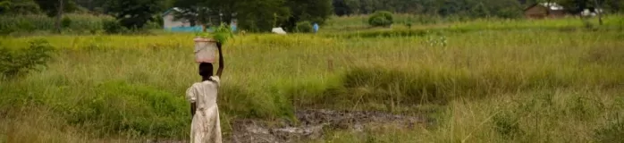 A young girl carries a bucket on her head, lightening her load