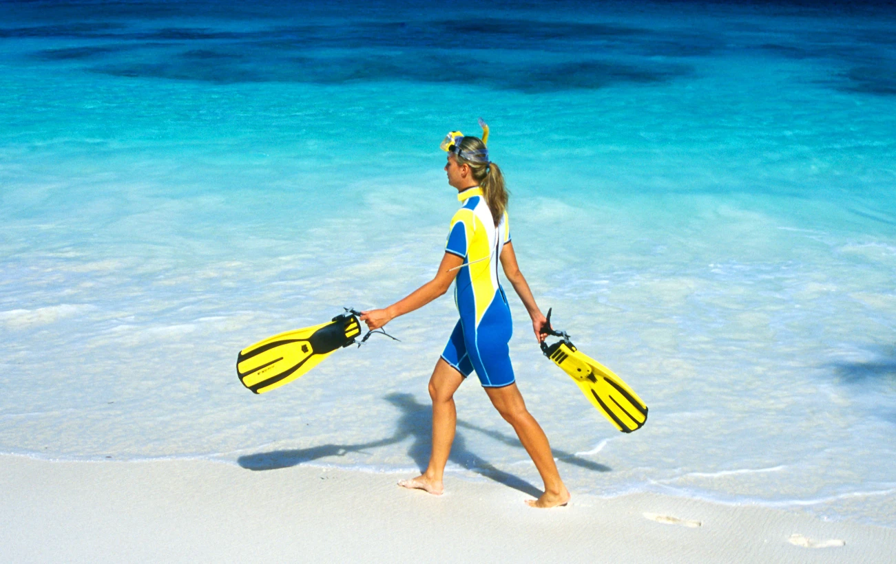 A snorkeler walking along a white sandy beach.