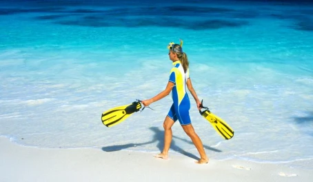 A snorkeler walking along a white sandy beach.