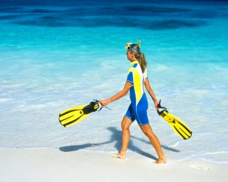 A snorkeler walking along a white sandy beach.