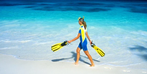 A snorkeler walking along a white sandy beach.