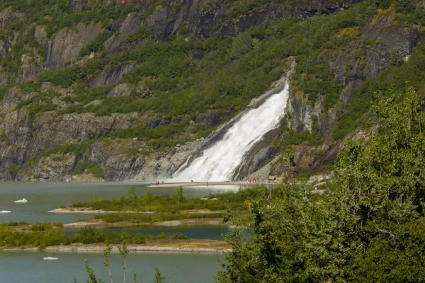 A large waterfall cascades from the Alaskan mountainside