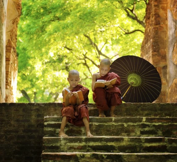 Two young monks read on the steps of a temple
