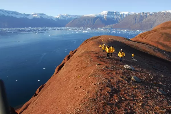 Hike along Eastern Greenland's red earth hills to gaze down at the iceberg-filled seas.