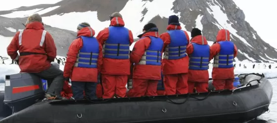 A group of travellers sail around a penguin colony off the shores of Antarctica