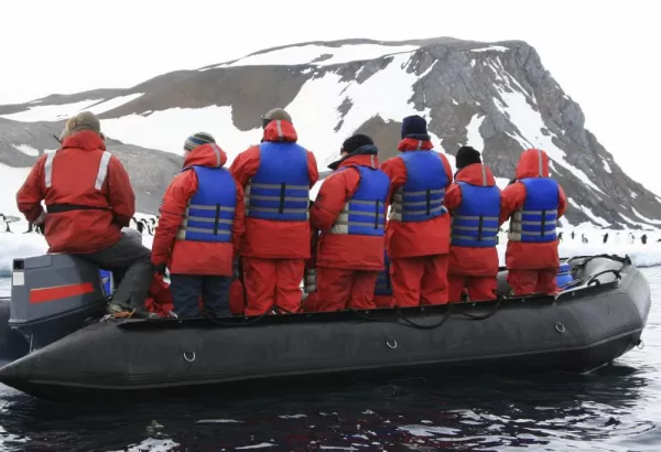 A group of travellers sail around a penguin colony off the shores of Antarctica